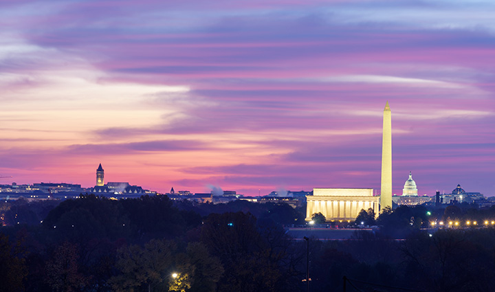 Panoramic view of Washington, DC at dusk with Capitol, Lincoln Memorial, and Washington Monument under a vibrant, colorful sky. 
