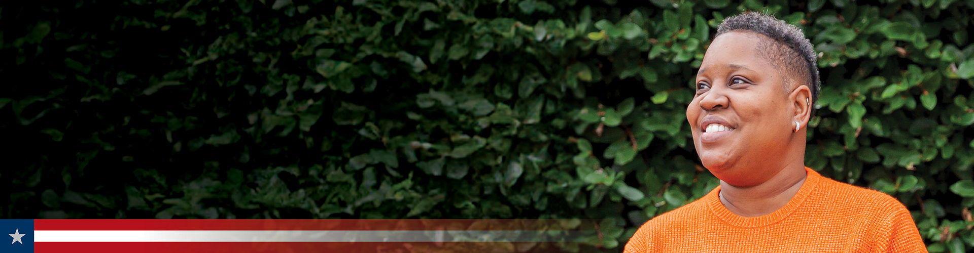 Wounded warrior Donna Pratt stands outside smiling. She has a short haircut and wears a bright orange textured sweater.