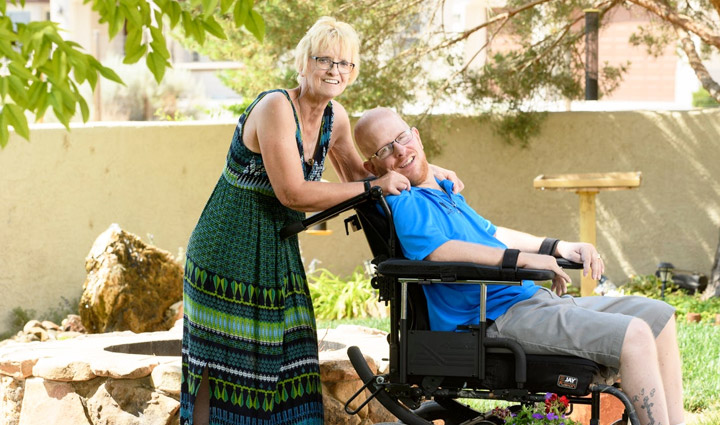 Caregiver Christine Schei and her son, wounded warrior Erik Schei in a wheelchair, smile while being outside.