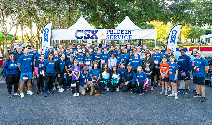 CSX employees standing under a CSX Pride in Service sign wearing blue t-shirts with CSX on them at WWP Carry Forward 5K.