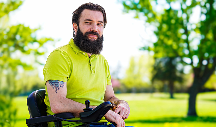 Wounded warrior Drew Carpenter sits outside while smiling and wearing a lime green polo shirt.