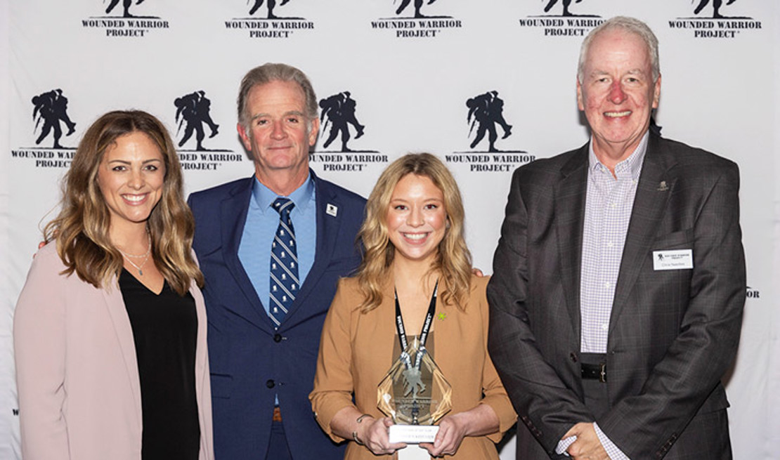 Parker’s Kitchen executive Lauren Burel holding the WWP award stands between WWP Staff Alexis Long and CEO Walt Piatt on the left and Chief Chris Needles on the right.