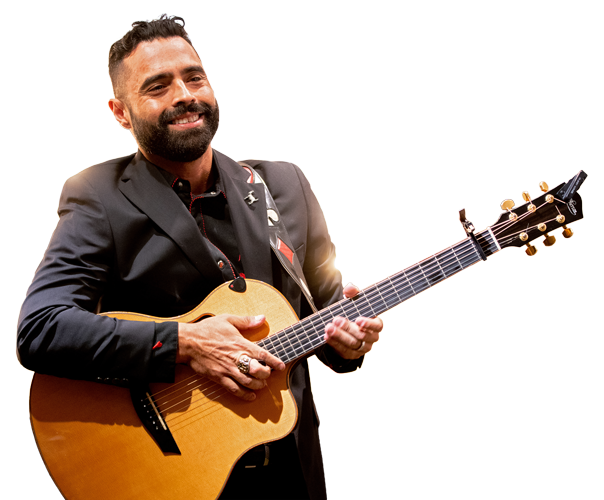 Warrior Sal Gonzalez smiles brightly while holding a guitar, dressed in a suit backstage at the Grand Ole Opry.