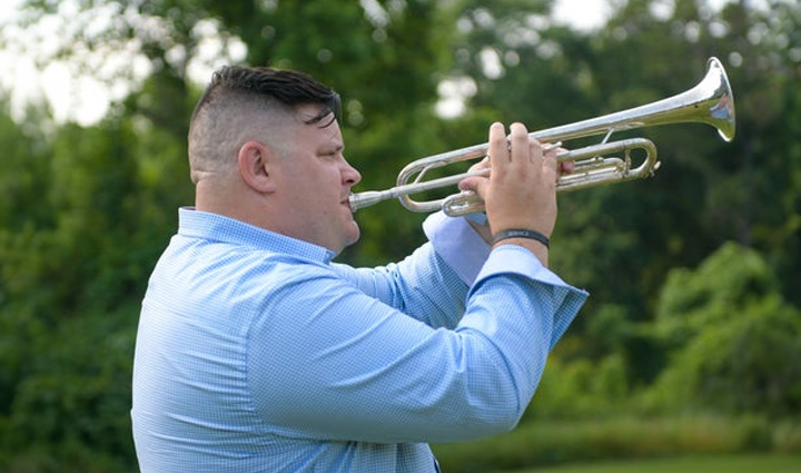 Warrior Jake Norostky is standing outside playing the trumpet.