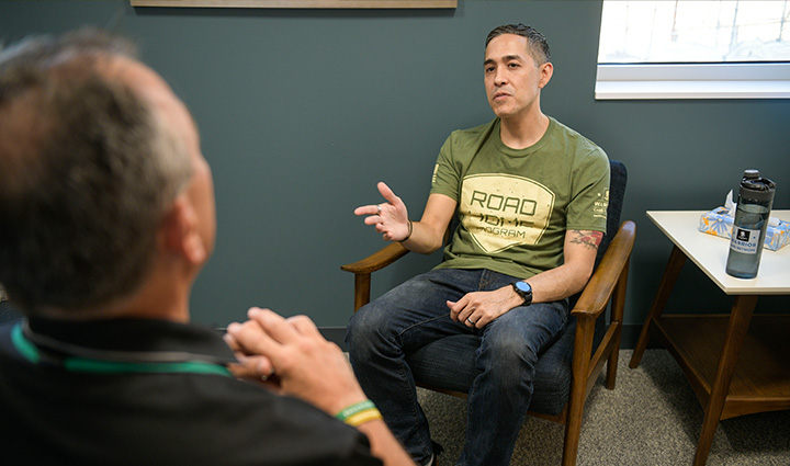 Wounded warrior Sergio Alfaro speaks with a clinician while sitting in a chair.
