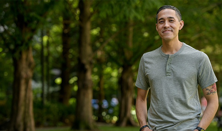 Sergio Alfaro outdoors in gray henley shirt and blue jeans with his hands in his front pockets.