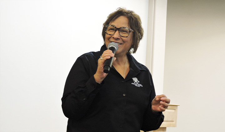 Caregiver Cindy Parsons smiles while speaking into a microphone at a past Warriors Speak event.
