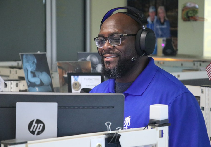 A WWP teammate smiles at his computer screen while listening to a call on his headset.