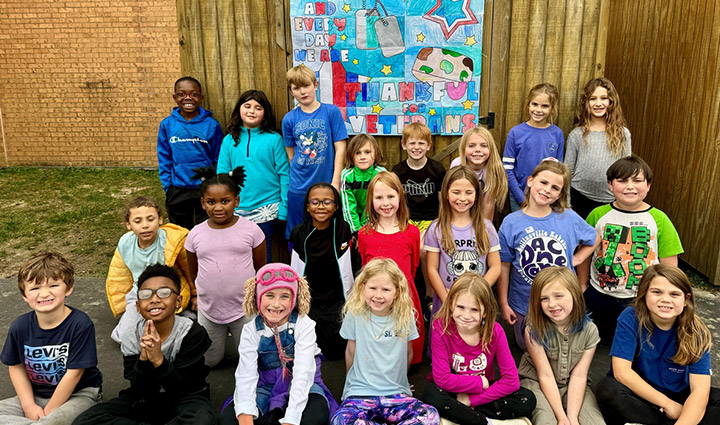Elementary school students pose with a handmade sign showing their appreciation for our nation’s veterans for Honor Their Courage.