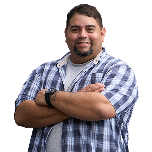 Warrior Tim Aponte smiles with his arms crossed while wearing a short sleeved plaid shirt and a watch on his left wrist.
