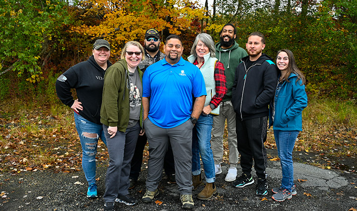 Wounded warrior Tim Aponte stands outside near trees with a group of seven male and female warriors. 