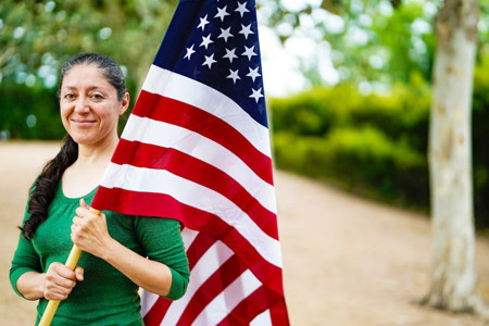 Warrior Ruth Corrigeux, holding an American flag, walks along a tree-lined path.