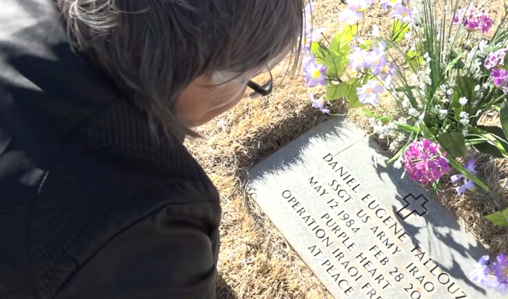 Mary Tallouzi, dressed in black, crouches down next to the gravestone of her son, Daniel, with flowers seen in the background.