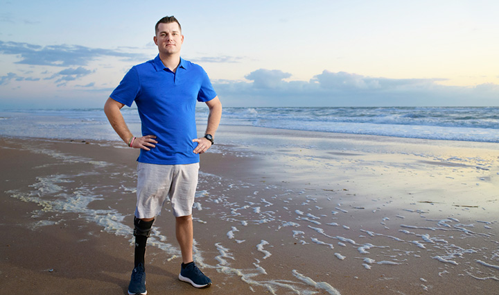 Wounded warrior Mike Larson stands on a sunset beach, proudly showcasing his prosthetic leg with confidence and pride.