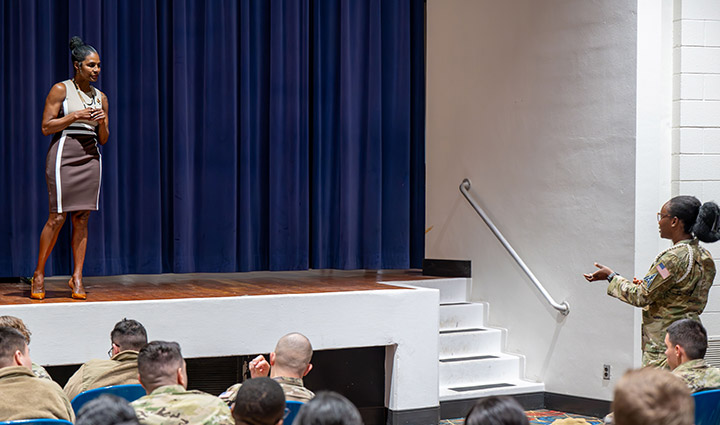 Wounded Warrior Tonya Oxendine stands on stage in a business dress and takes questions from a Space Force uniformed female warrior in the audience during a speaking engagement.