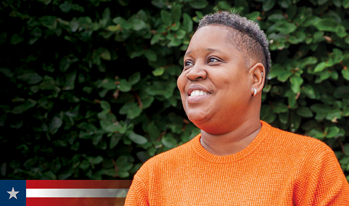 Wounded warrior Donna Pratt stands outside smiling. She has a short haircut and wears a bright orange textured sweater.